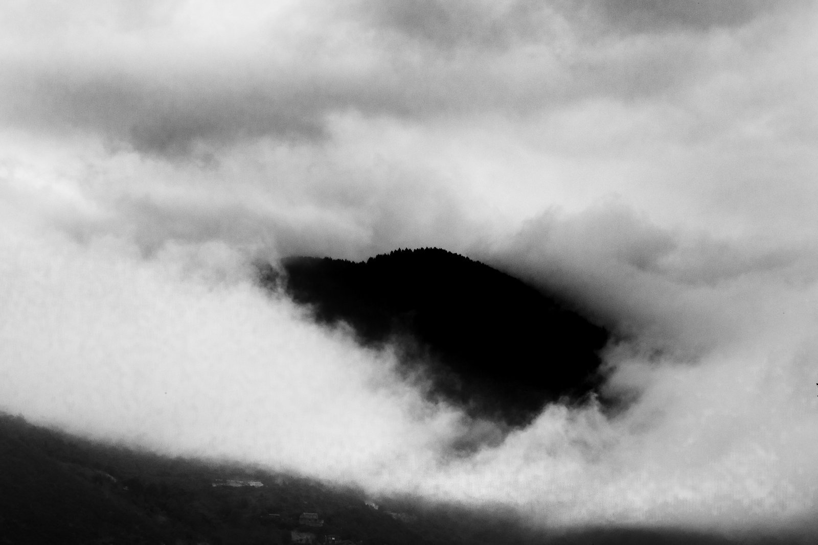 A dark mountain peak emerging from thick fog, in black and white